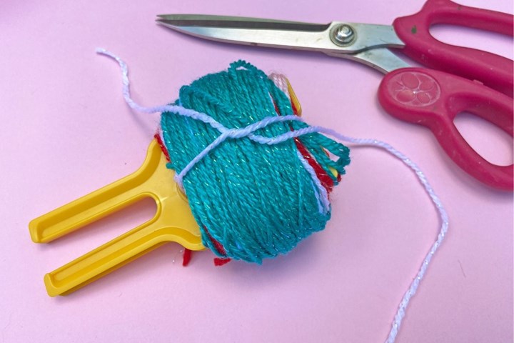 Cut about 30cm of yarn of any colour. Thread through the bottom of the U shape on your pom-pom maker and bring it around to tie in a loose knot.
