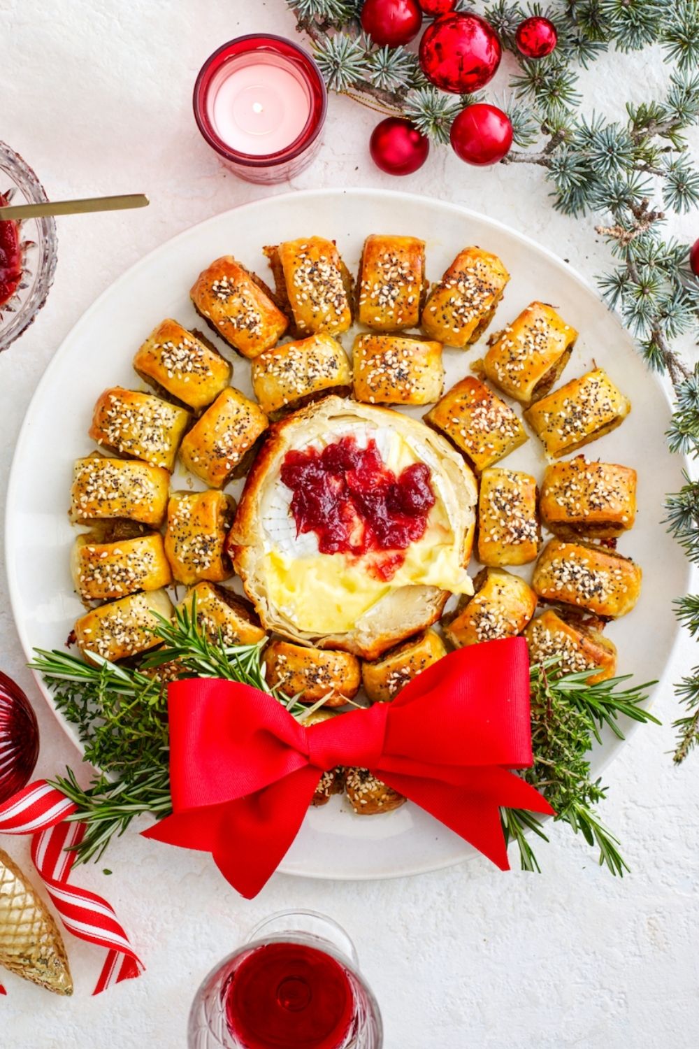 sausage roll wreath with camembert shaped in a circle around camembert with rosemary and large red bow